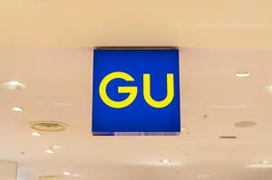 Sign with "GU" logo hanging from a store ceiling in a shopping mall