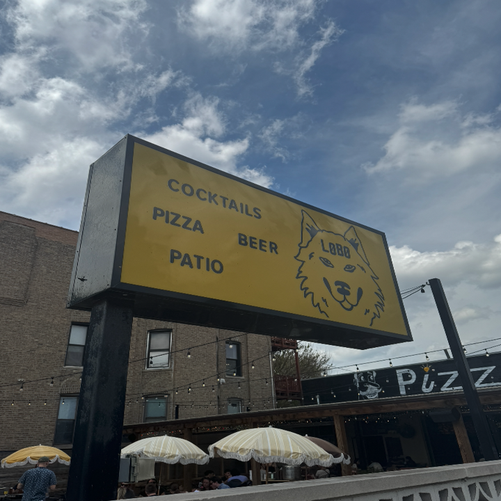 Sign for a restaurant featuring cocktails, pizza, beer, and patio seating with a drawing of a wolf's head