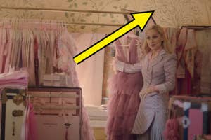Emily in Paris: Emily stands in a closet, holding a pink dress on a hanger, surrounded by various clothes and wardrobe items