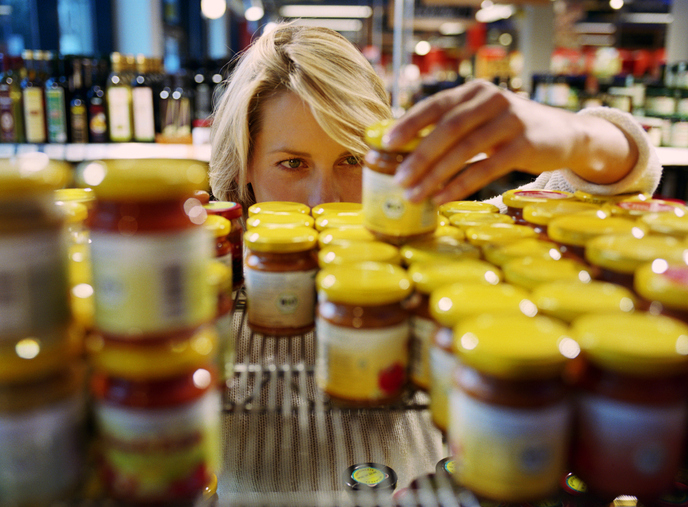 A person is organizing jars of food on a supermarket shelf, focusing on arranging them neatly
