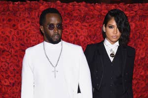 Sean “Diddy” Combs and Cassie Ventura pose together, with Diddy in a white suit and Cassie in a black suit at a red-carpet event, against a backdrop of red roses