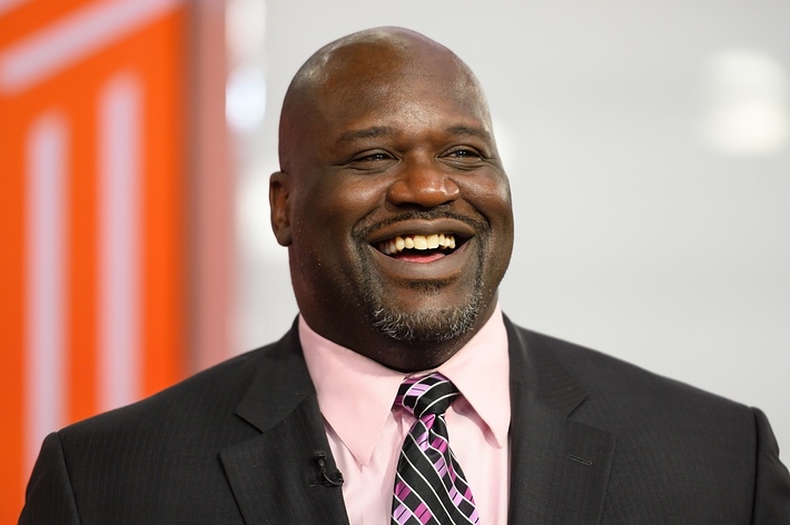 Shaquille O'Neal smiling and wearing a dark suit, a pink shirt, and a patterned tie