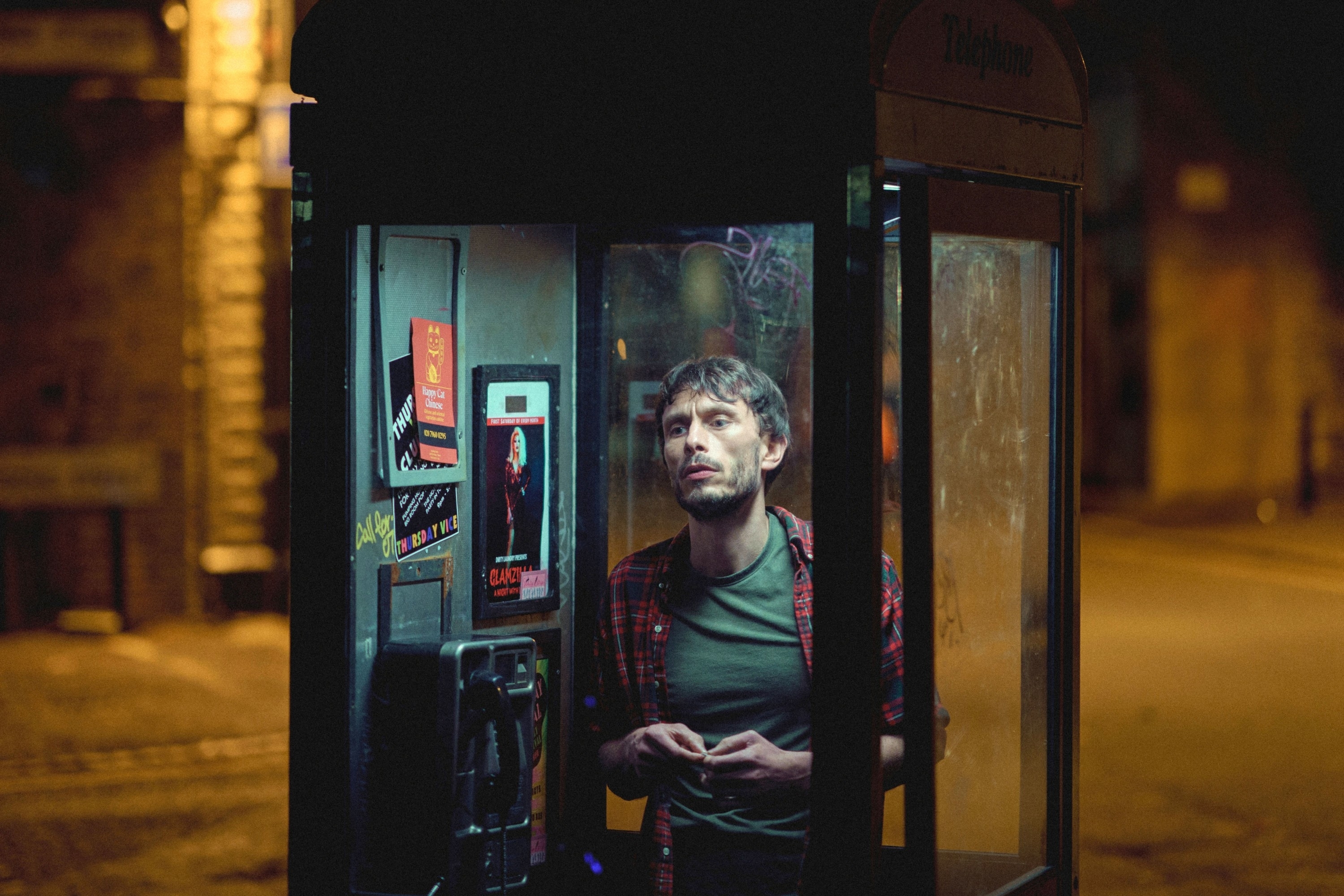 Richard Gadd in a checkered shirt inside phone booth at night