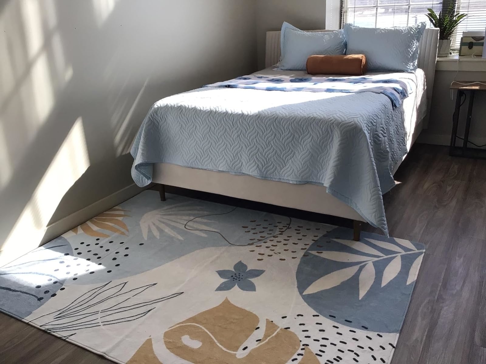 Bed with a blue patterned bedspread on a modern rug in a sunlit room, suggesting home decor styles