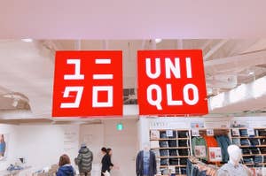 店内に掲げられた「ユニクロ」と書かれた2つの赤い看板。店は衣服を陳列した状態で人が買い物をしています。