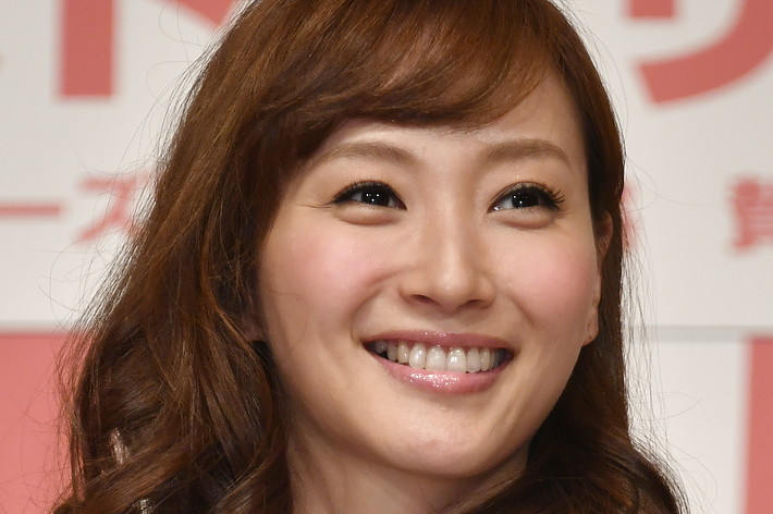 広告記事用：グレーのトップスを着た女性が笑顔でカメラを見ています。背景には「トーサツ」という文字があります。