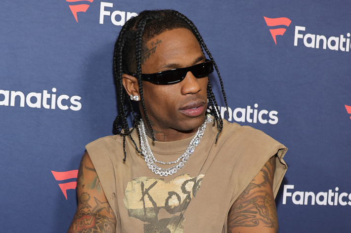 Travis Scott in a sleeveless, ripped T-shirt with chains and sunglasses at a Fanatics event
