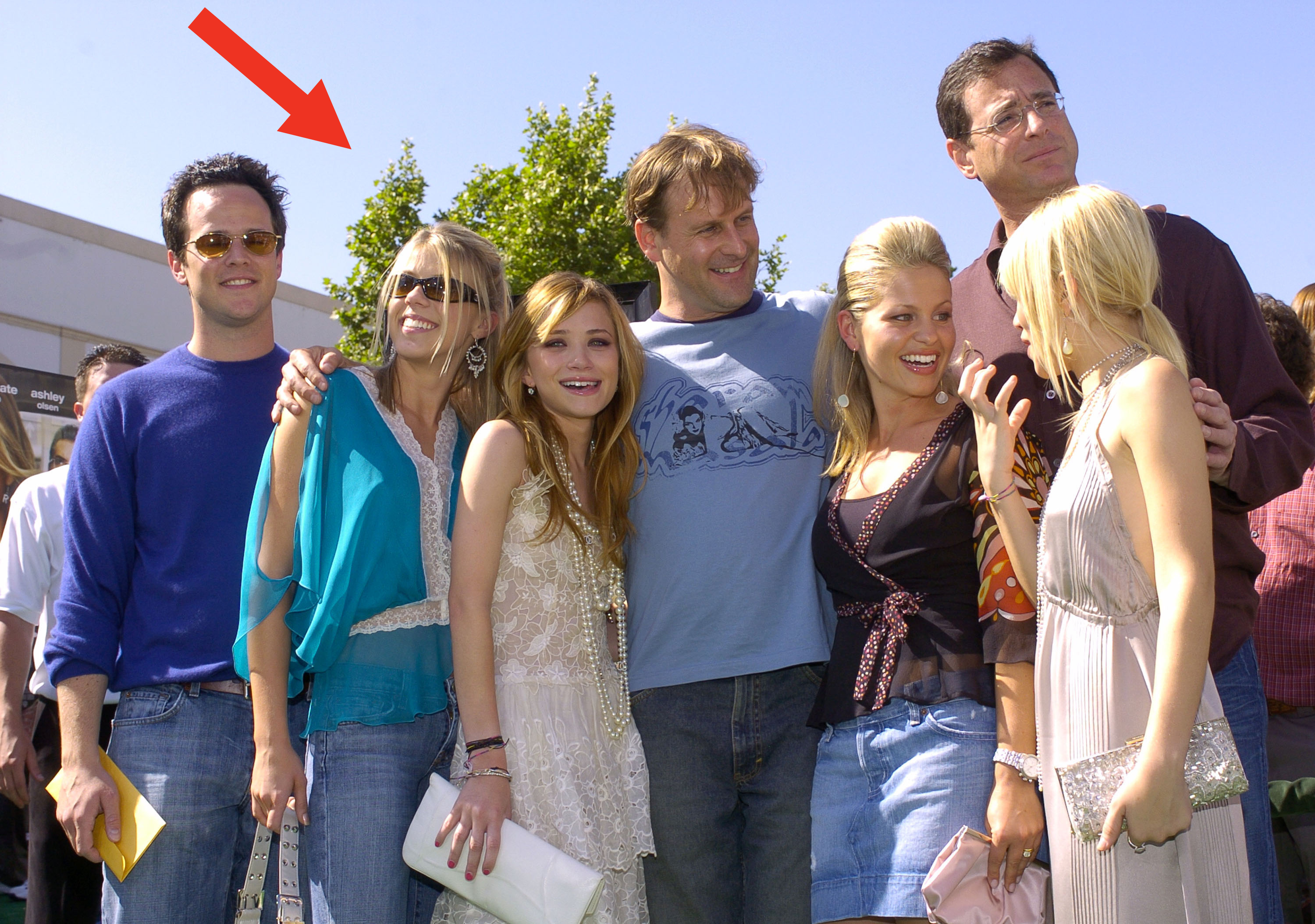 Cast of Full House posing together outdoors, including Dave Coulier, Jodie Sweetin, Mary-Kate Olsen, Ashley Olsen, Andrea Barber, Candace Cameron Bure, and Bob Saget