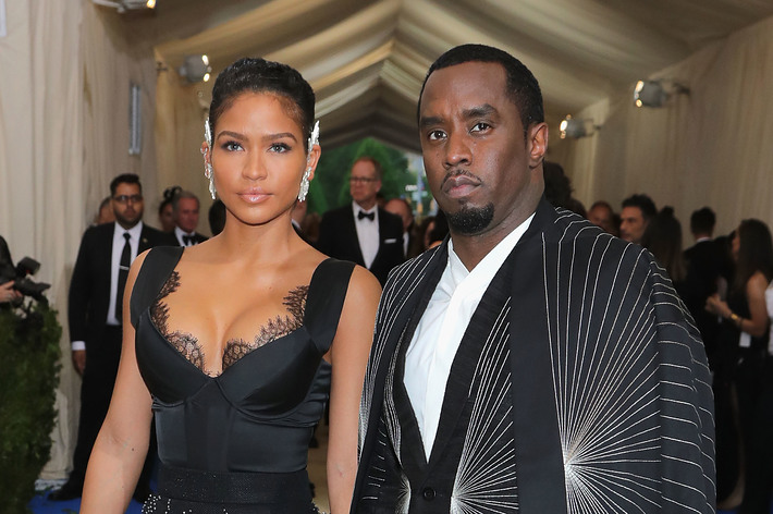 Cassie and Diddy pose on the red carpet. Cassie wears a plunging black dress with bead details, while Diddy wears an elaborate black and white suit with a sunburst pattern