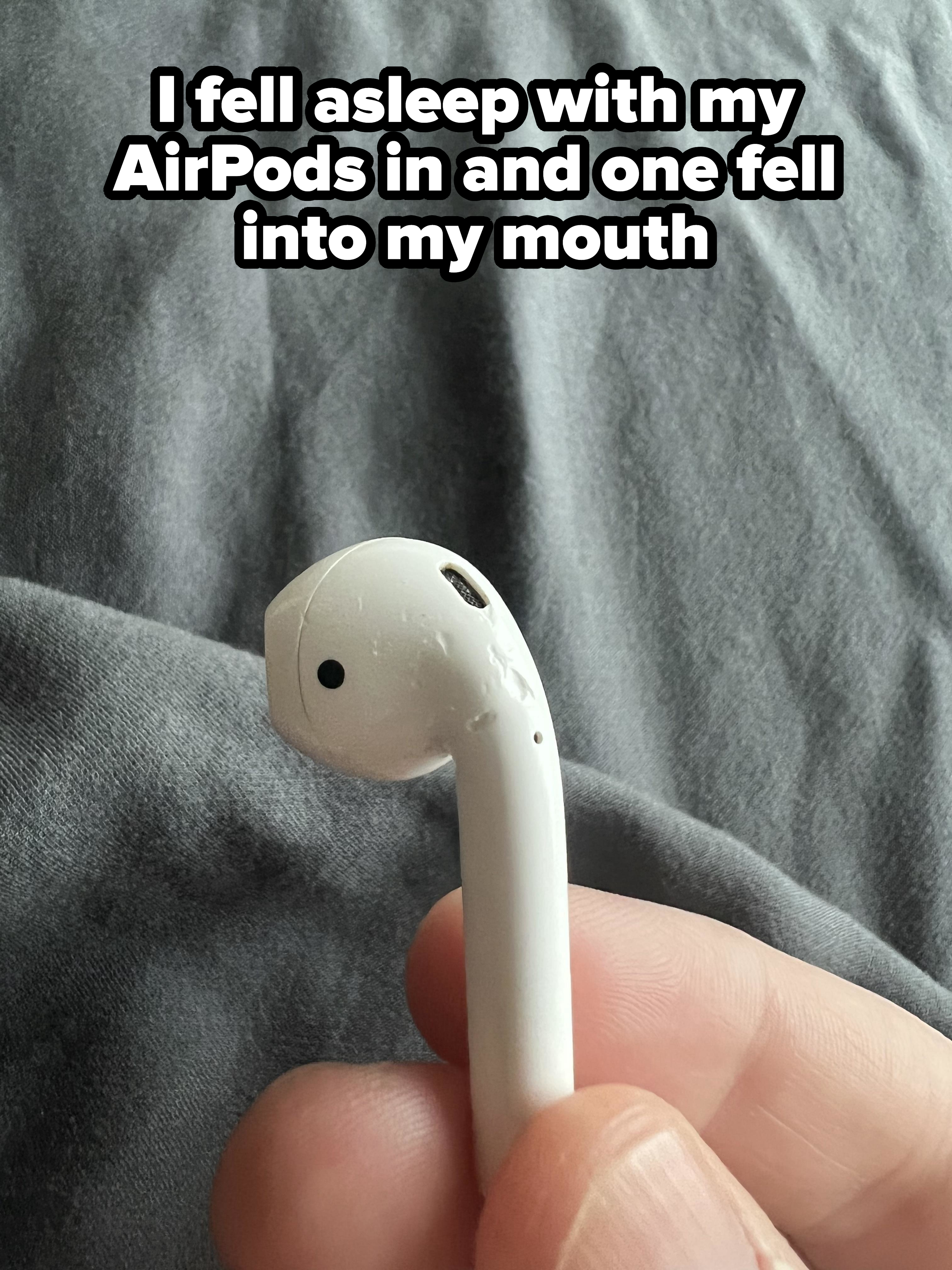 A close-up of a hand holding an Apple AirPod, showing its damaged and dirty microphone mesh