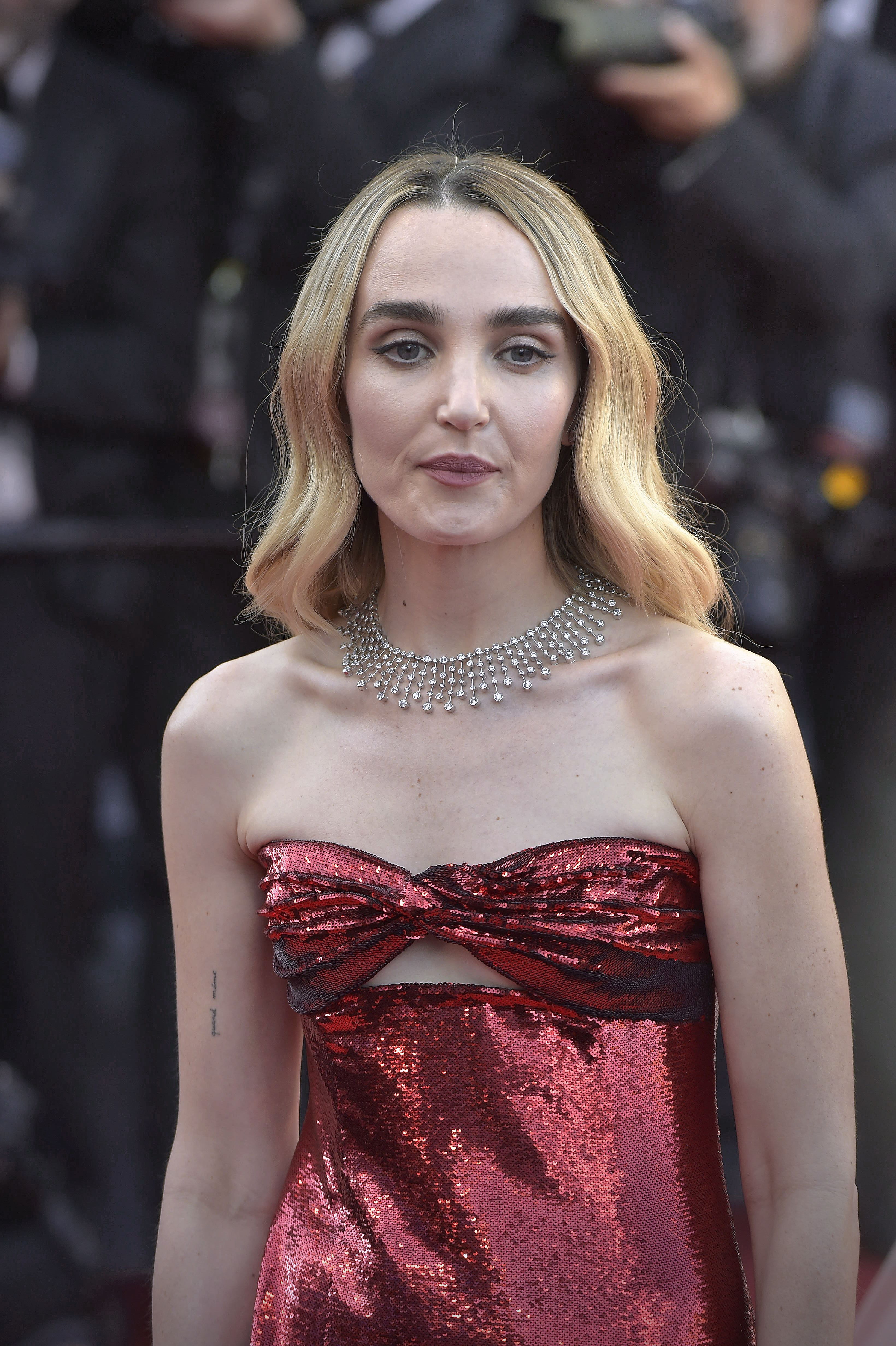 Chloe Fineman in a shimmering red strapless dress with a cutout at the chest and a pearl statement necklace at a red carpet event