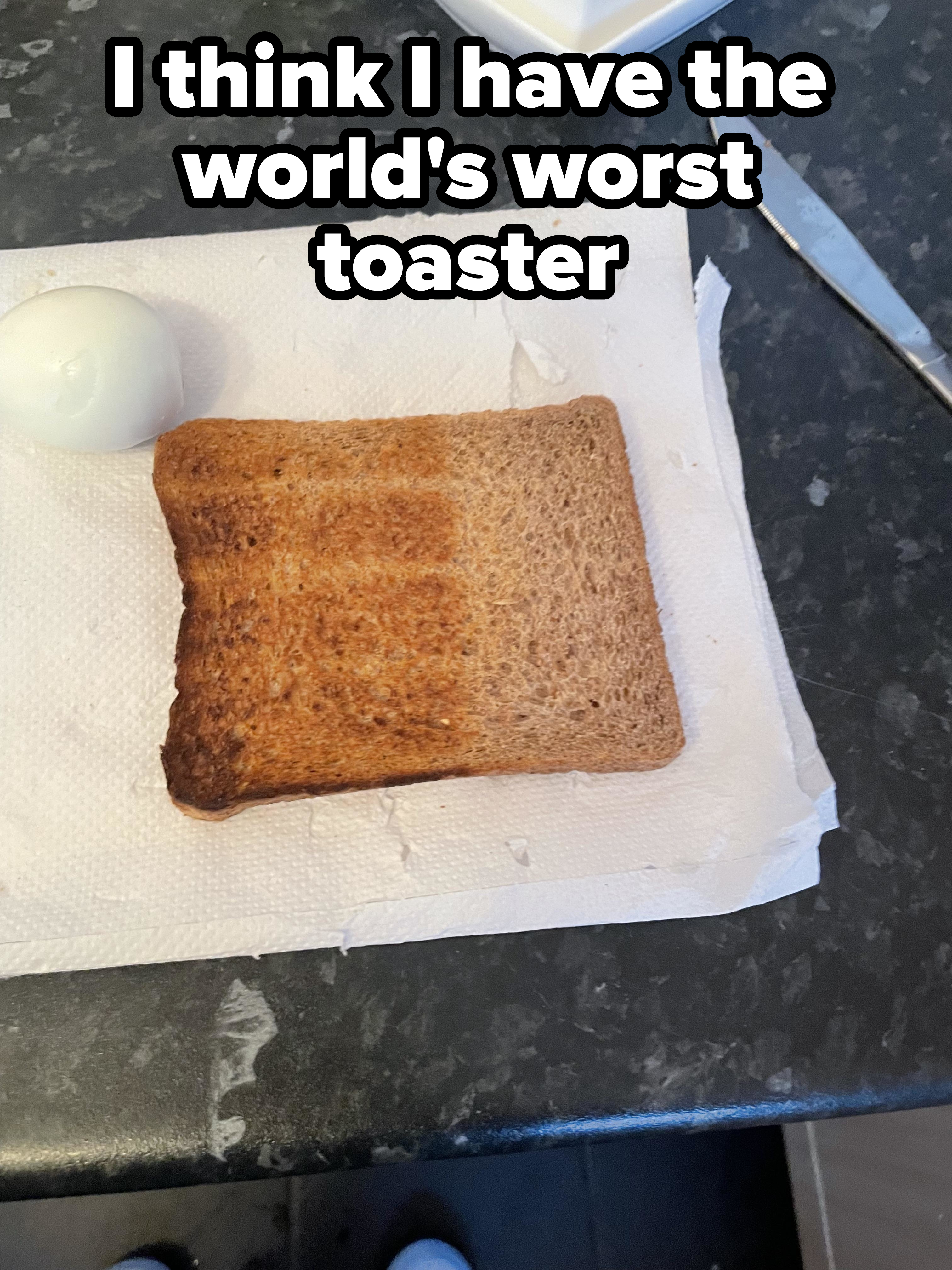A slice of toasted bread and a boiled egg placed on a paper towel on a dark countertop, with a butter knife nearby