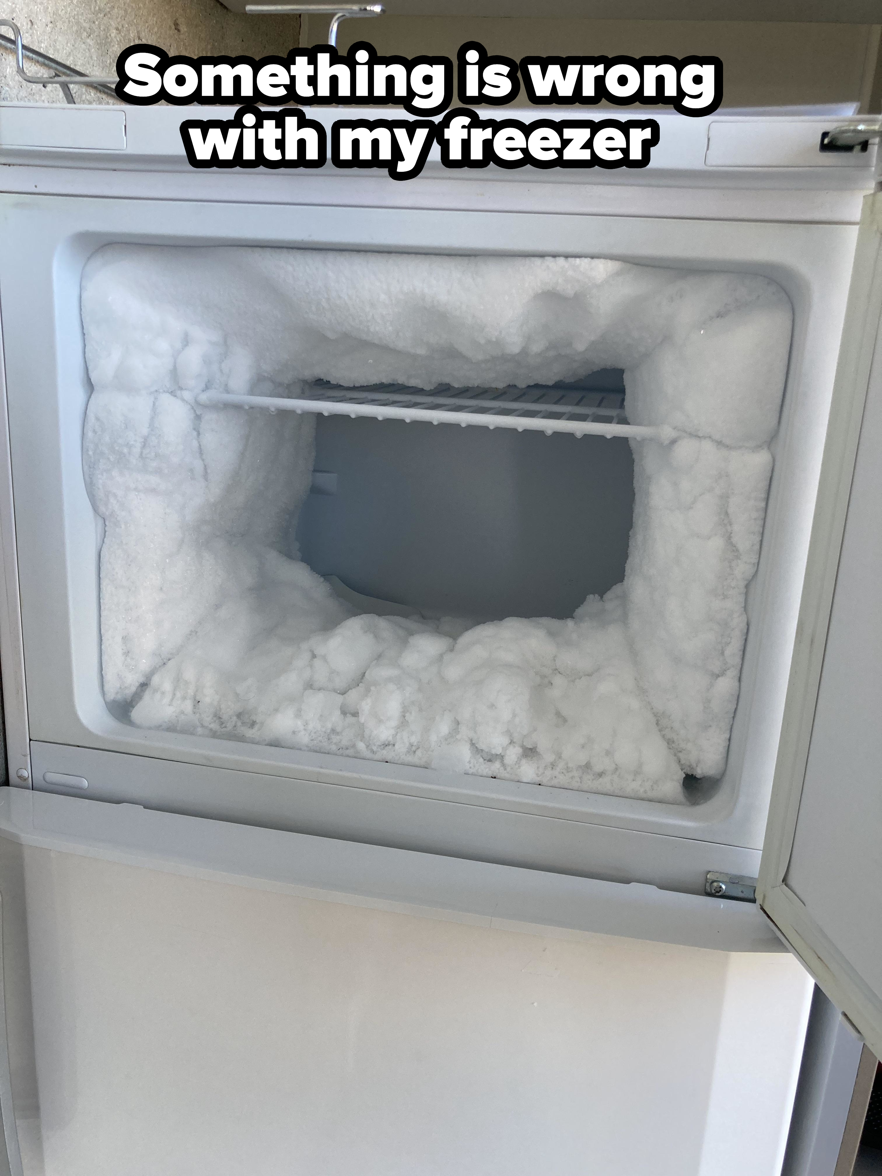 An open freezer door reveals significant ice buildup inside, blocking the interior space and shelves