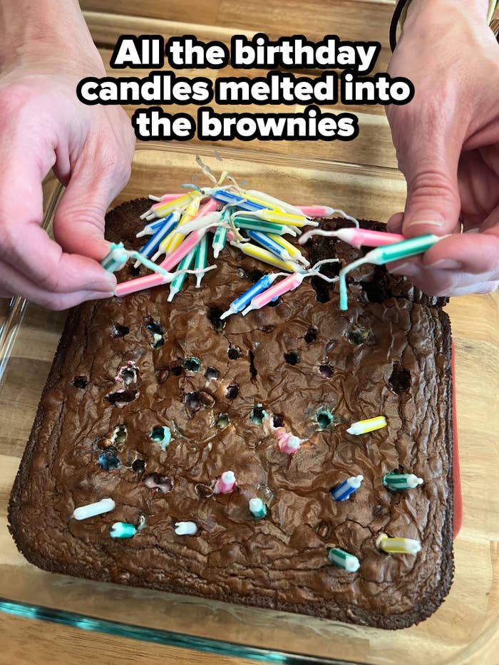 Close-up of hands removing a bunch of melted birthday candles from a chocolate brownie