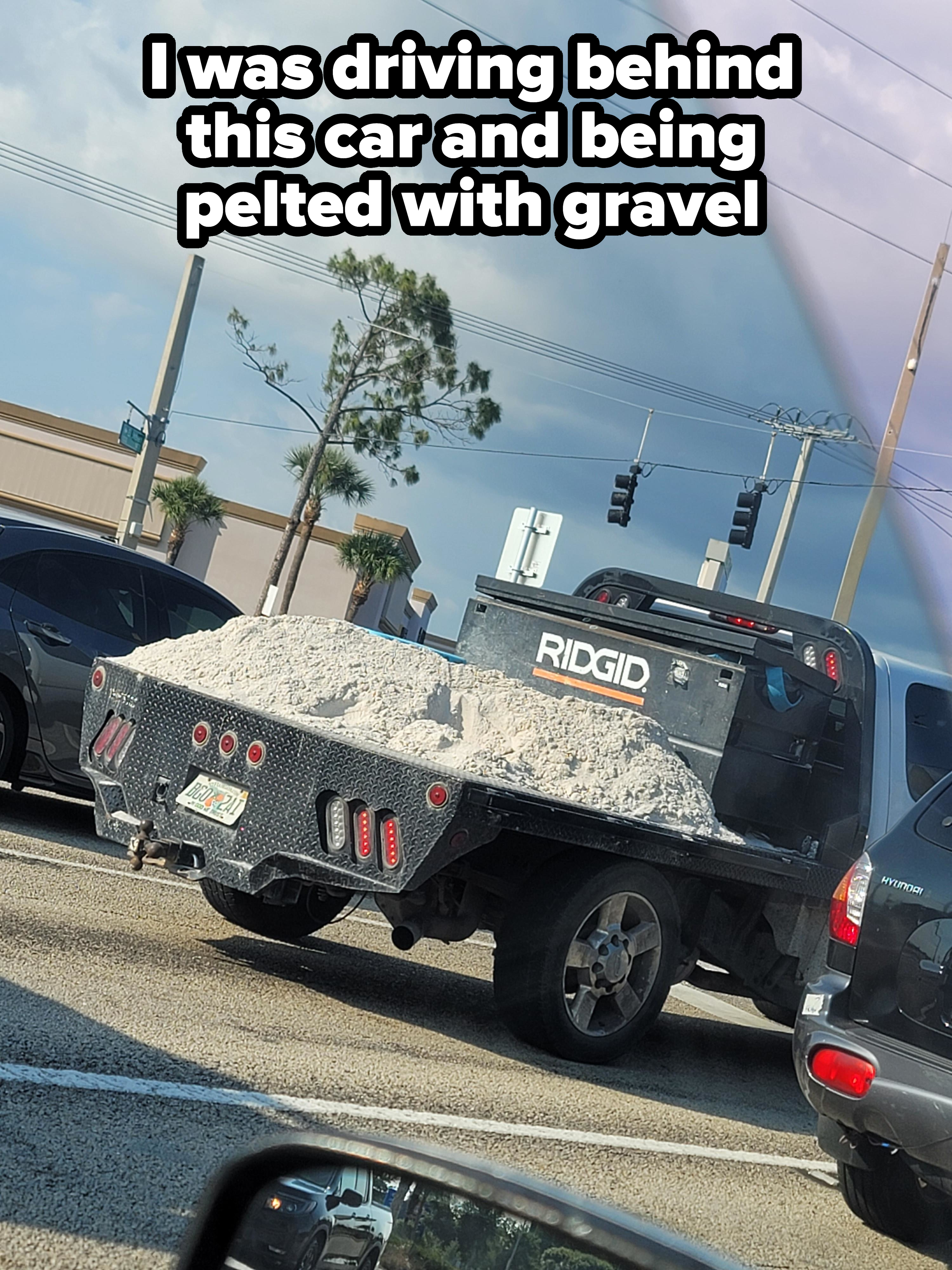Pickup truck on a city street carries a large load of gravel or sand in the back. RIDGID tool storage box is mounted on the truck's bed