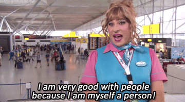 A person in a teal uniform with a name tag and lanyard is at an airport, saying, "I am very good with people because I am myself a person!"