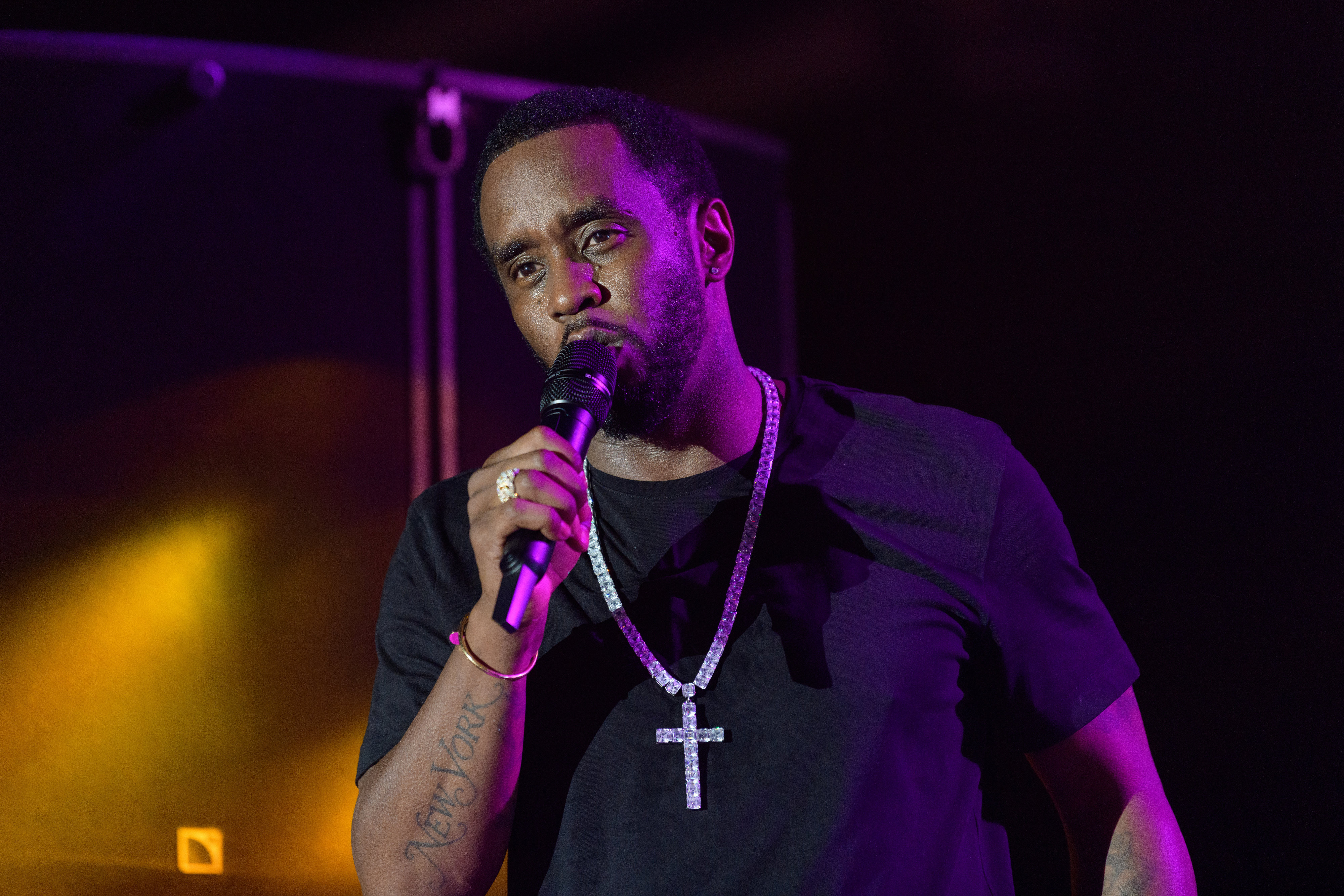 Sean &quot;Diddy&quot; Combs holds a microphone on stage, wearing a black shirt and a large jeweled cross necklace