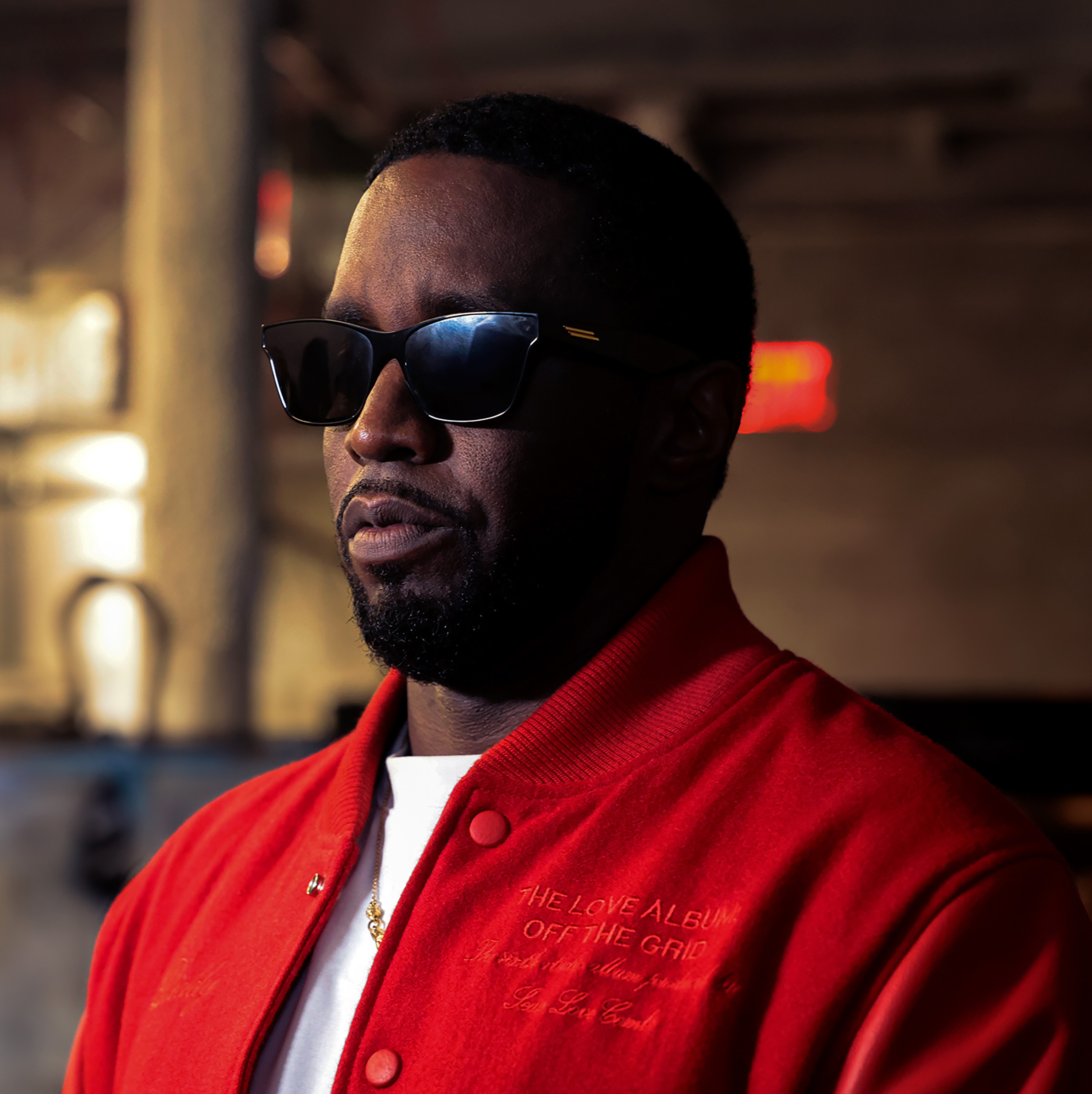 Sean "Diddy" Combs wearing sunglasses and a red jacket in a dimly lit setting