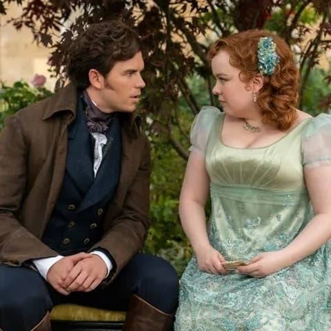 Jonathon Bailey and Nicola Coughlan in period costume. Jonathon wears a brown coat and Nicola a green dress with sheer sleeves and a floral hair accessory