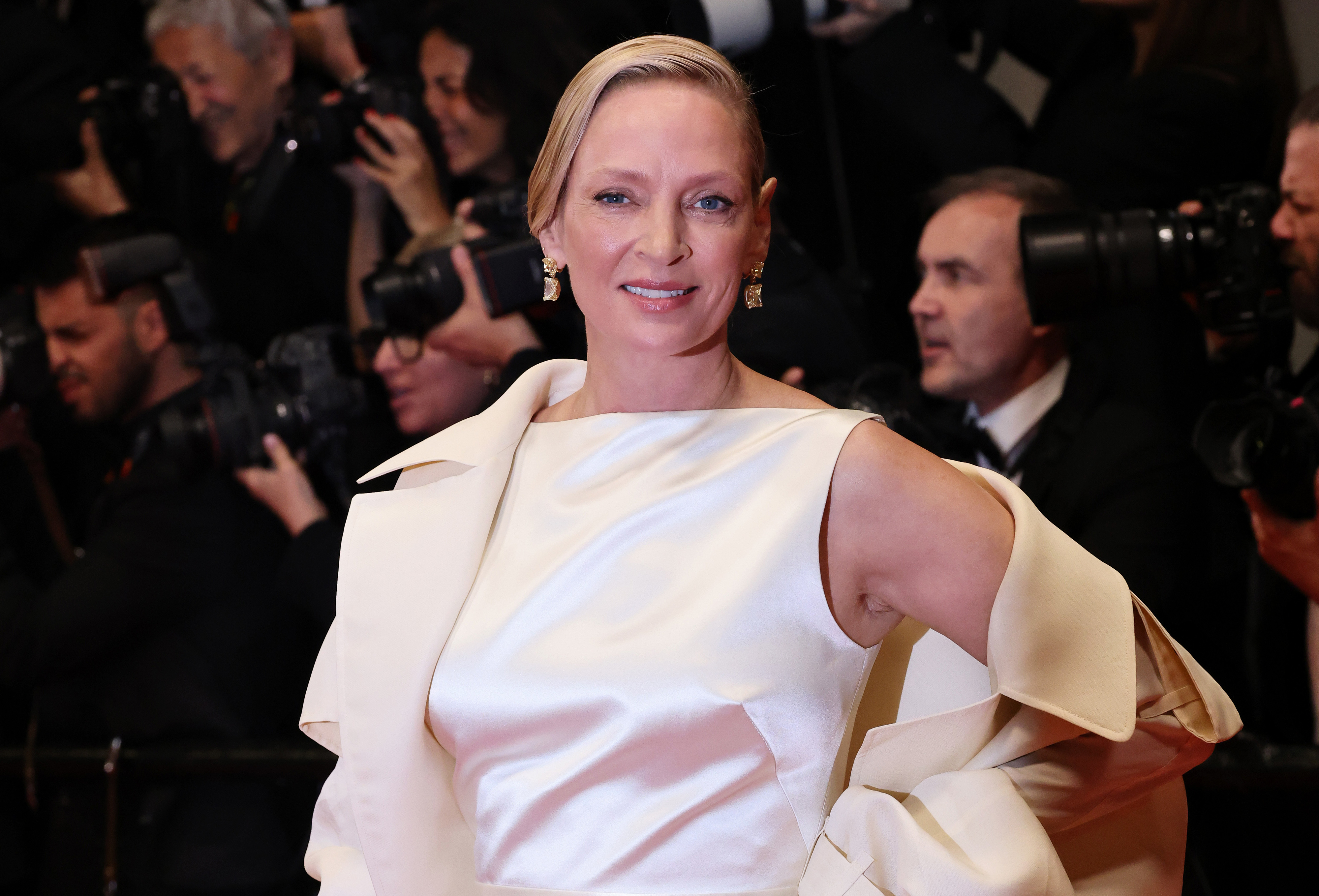 Uma Thurman posing elegantly on the red carpet, wearing a sophisticated gown, surrounded by paparazzi and photographers