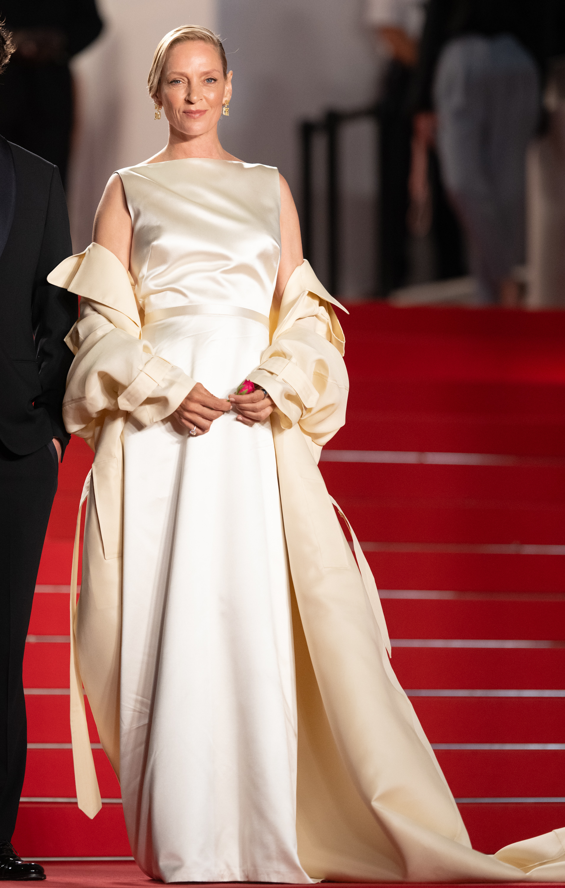 Uma Thurman in an elegant cream gown with draped sleeves, posing on a red carpet