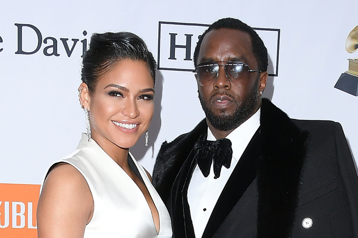 Cassie Ventura and Sean "Diddy" Combs at a red carpet event, standing together, smiling. Cassie is in a white gown, and Diddy is in a black tuxedo with a bow tie