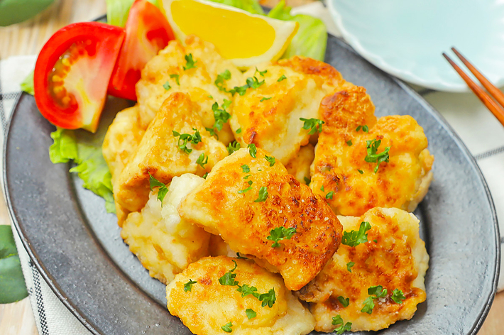 おいしそうな魚のフライが盛り付けられたプレート。トマト、レモン、レタスも添えられている。ビールの入ったグラスが後ろに見える。