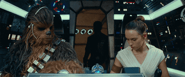 Chewbacca and Rey in the Millennium Falcon cockpit with controls and screens in the background