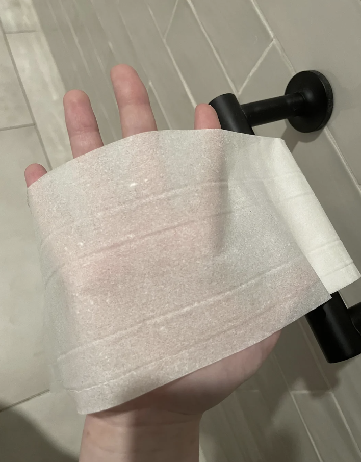Hand with a translucent toilet paper roll held up, seemingly insufficient in thickness