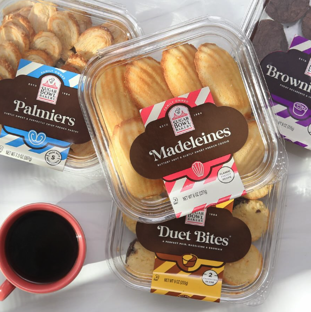 Various packaged baked goods, including palmiers, madeleines, and duet bites, with a cup of coffee