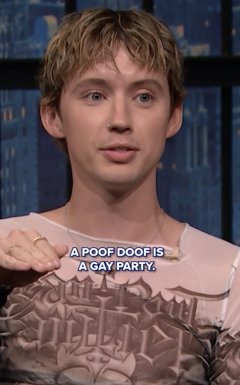 Person on a talk show wearing a graphic shirt with text overlay: &quot;A POOF DOOF IS A GAY PARTY.&quot;
