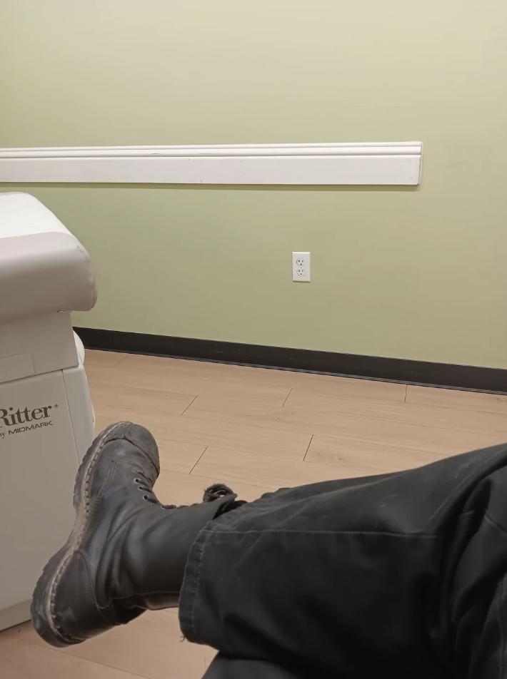 Person&#x27;s feet in boots resting on a medical examination bed in a room