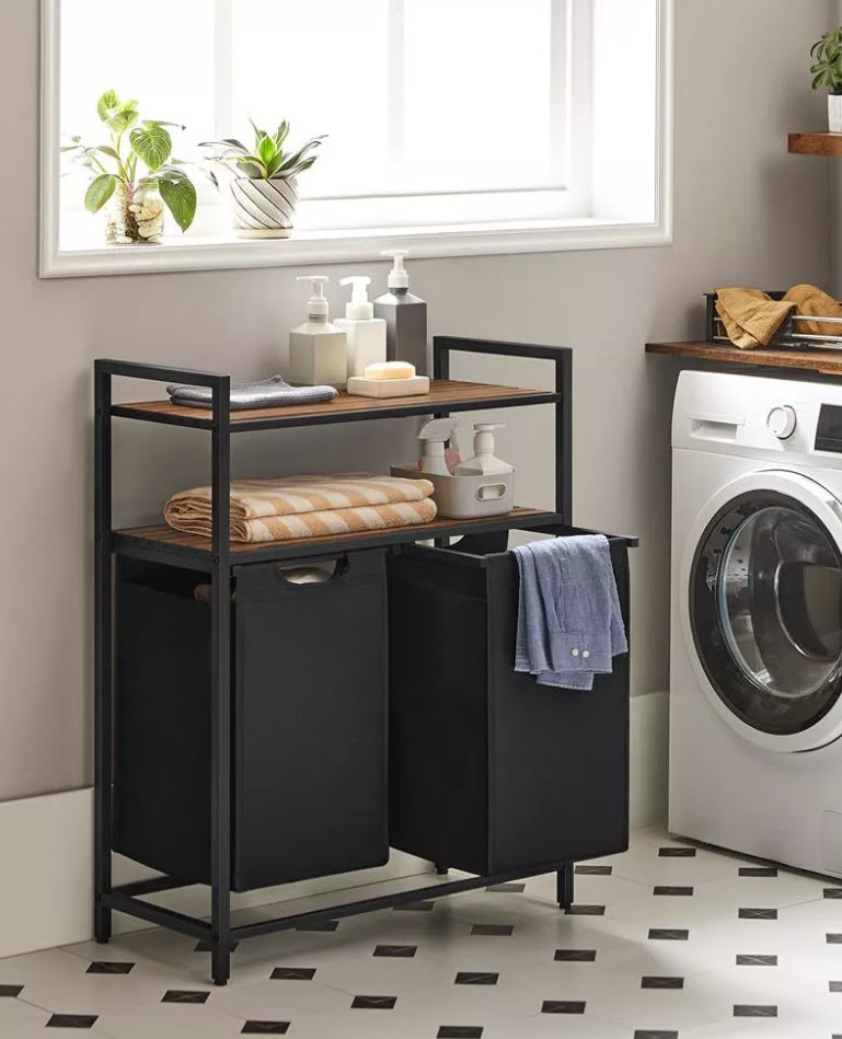 Laundry room with a washing machine, shelving unit with towels and containers, and two black bins