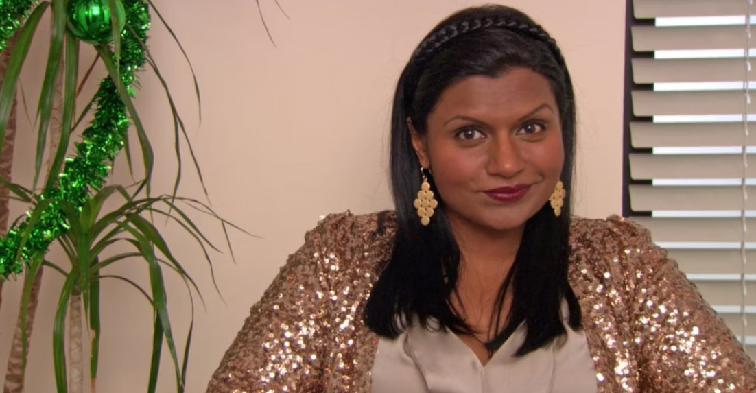 Mindy Kaling as Kelly Kapoor in 'The Office' wearing a sequined top, sitting in an office setting