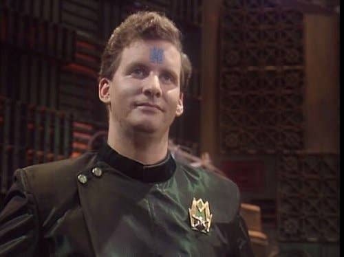 Character Rimmer from Red Dwarf with a hologram &#x27;H&#x27; on his forehead, in a military-style jacket