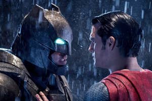 Batman and Superman face each other closely, showing tension, in a rainy scene. They appear as their iconic characters