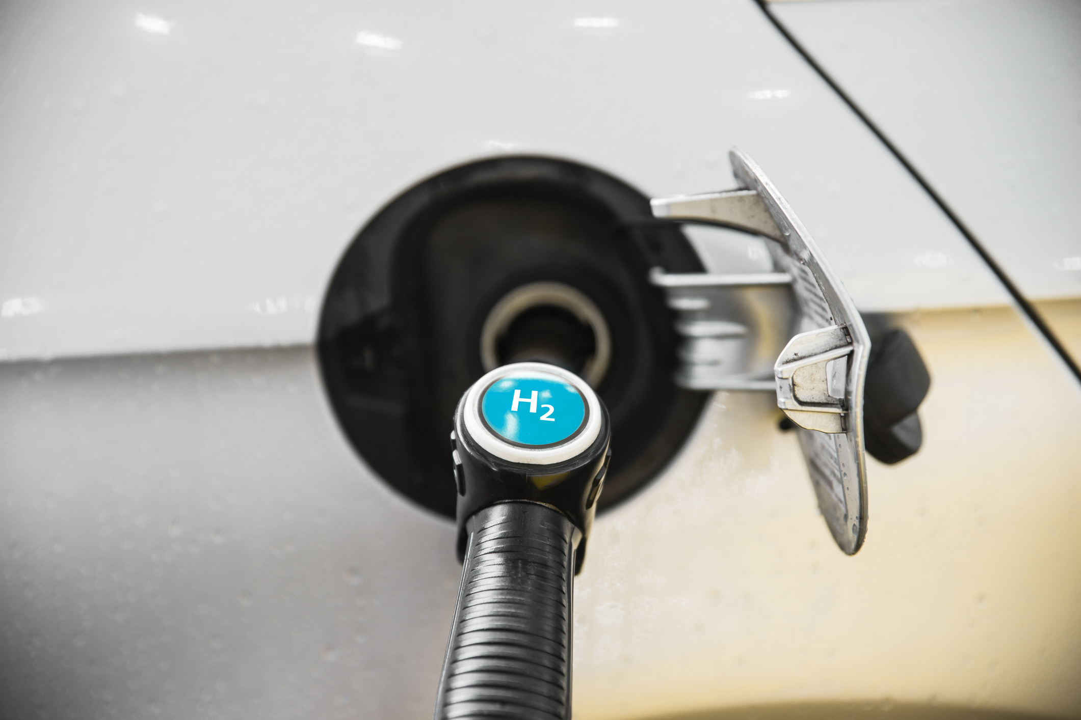 A car being fueled at a hydrogen station, nozzle attached to car's tank with H2 label visible