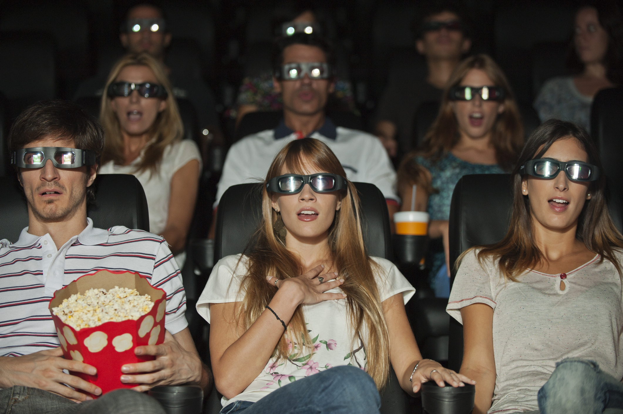 Audience in 3D glasses watching a movie, expressions of surprise, one holding popcorn