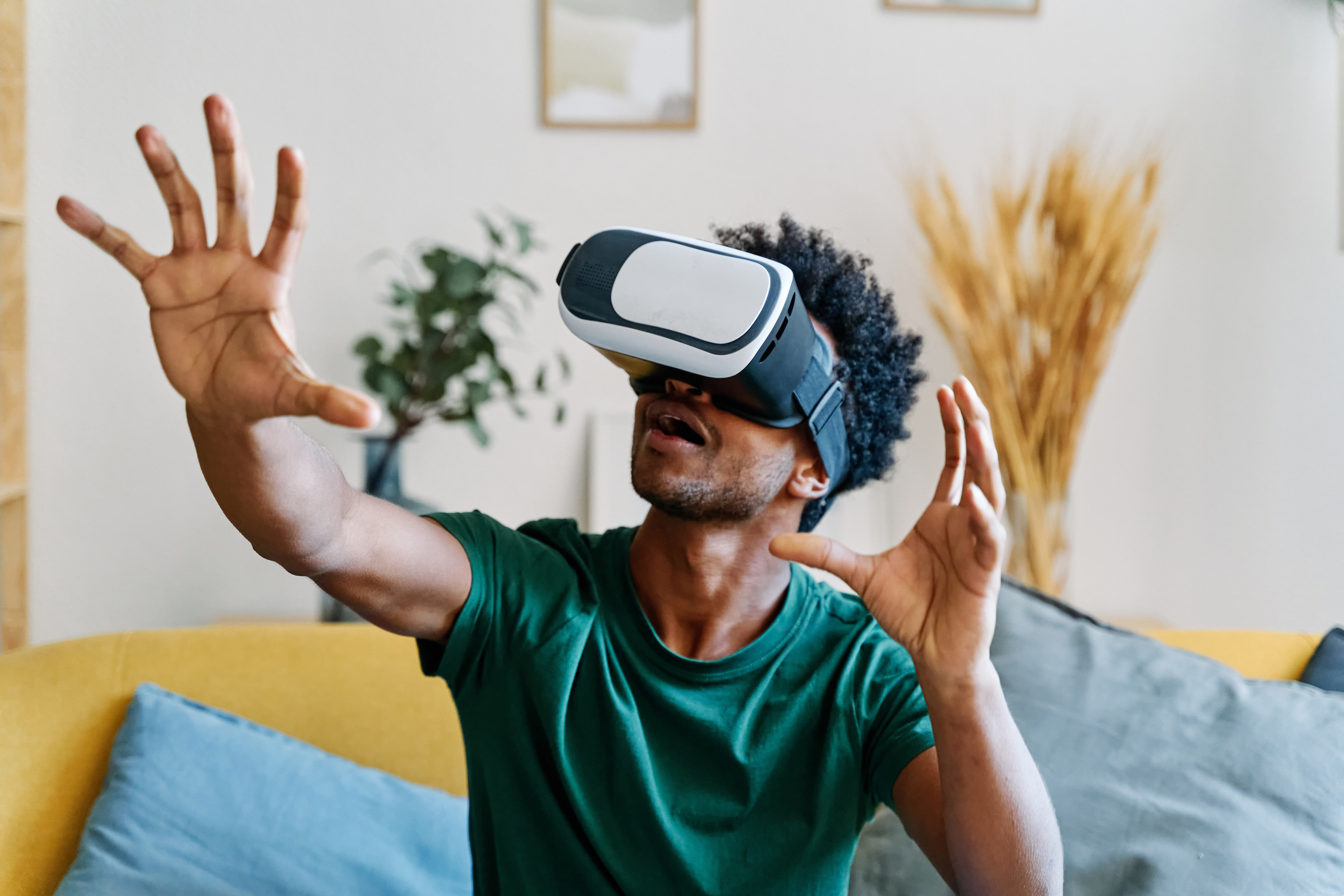 Person in a VR headset reaching out with hands, seated on a couch, seemingly immersed in a virtual experience