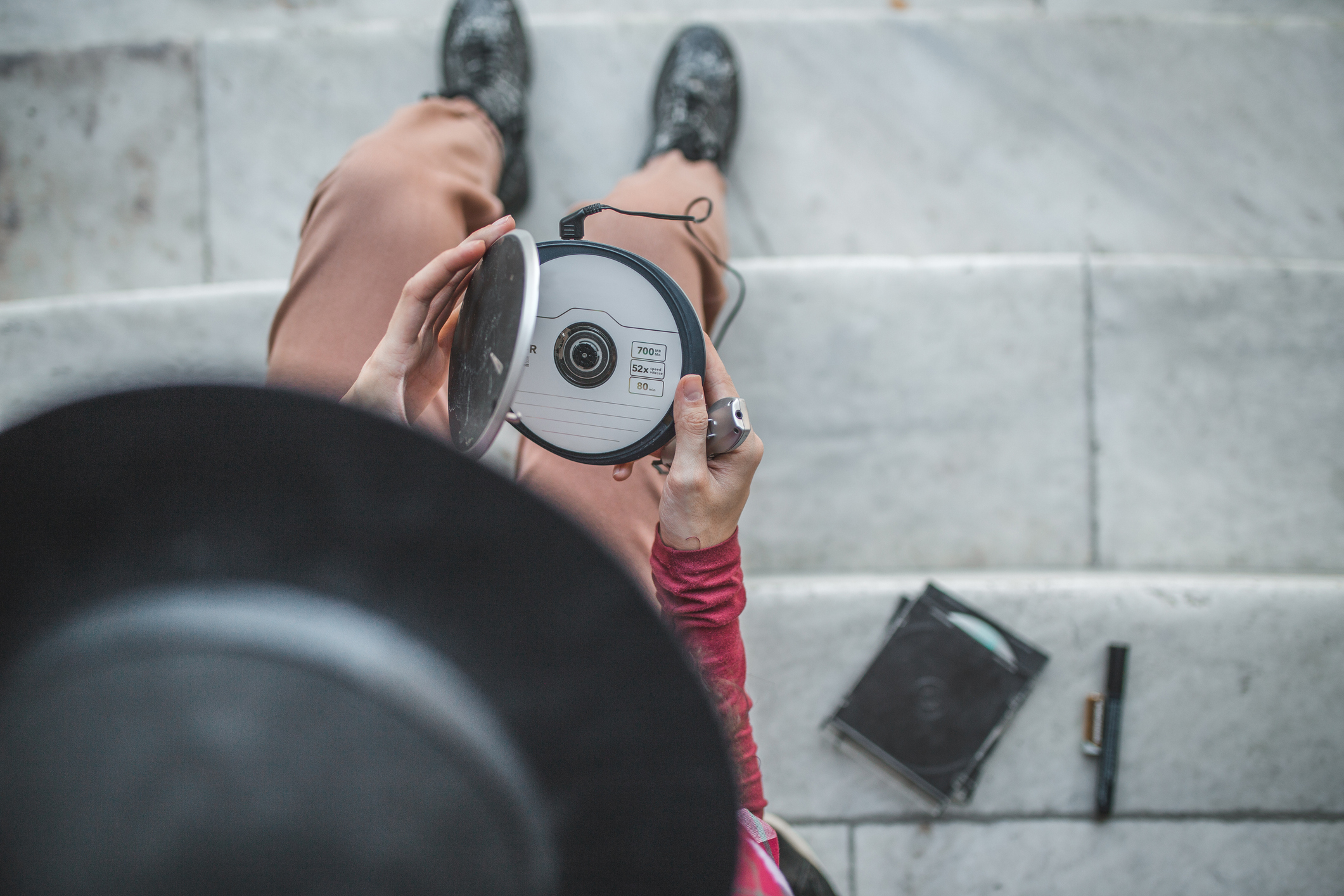 Person sitting on stairs holding a camera, with a notebook and pen beside them