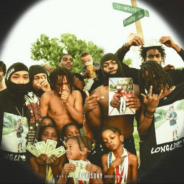 Group of individuals posing with cash & album cover, with children in front, in an outdoor setting
