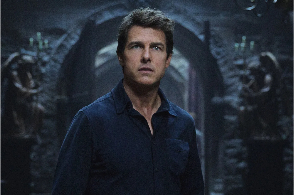Tom Cruise in a dark shirt, with a concerned expression, standing in an eerie setting with Gothic architecture