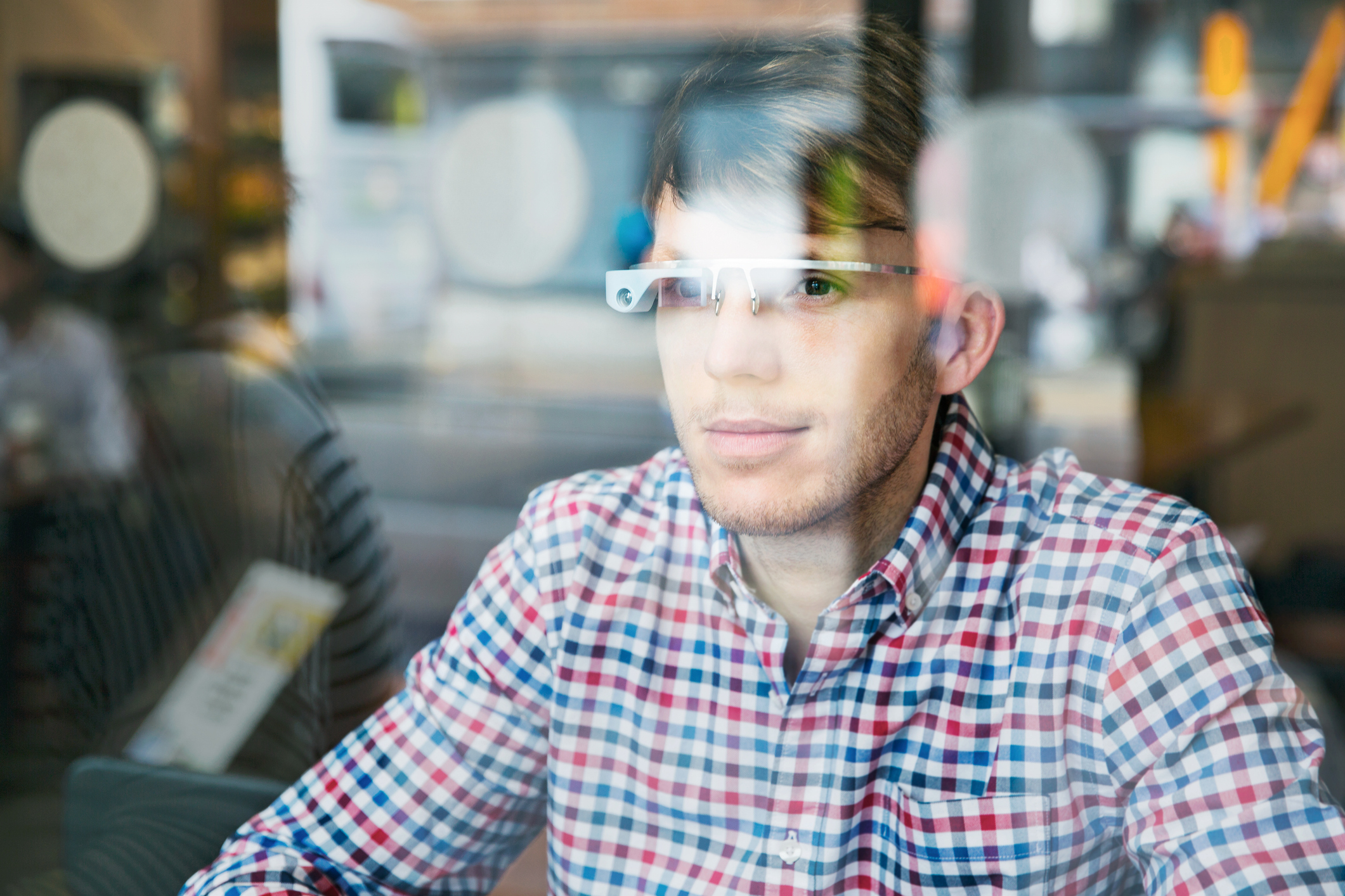 Person in a plaid shirt wearing smart glasses, looking through a window with reflections