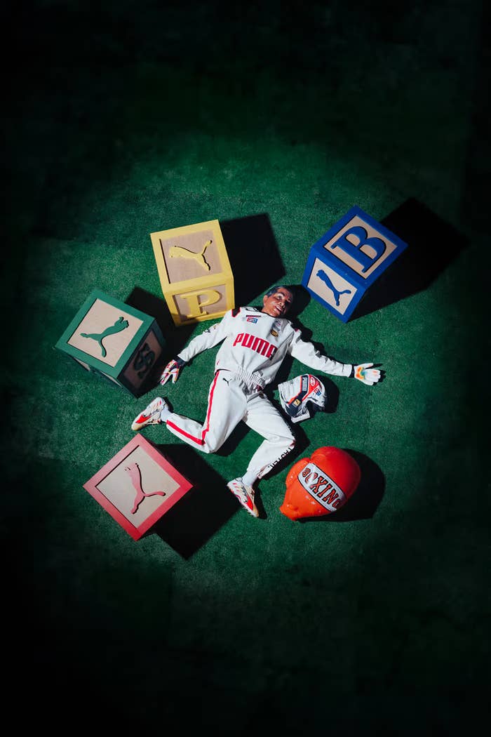 Person lying surrounded by oversized Puma sneaker boxes, wearing a white tracksuit with Puma branding