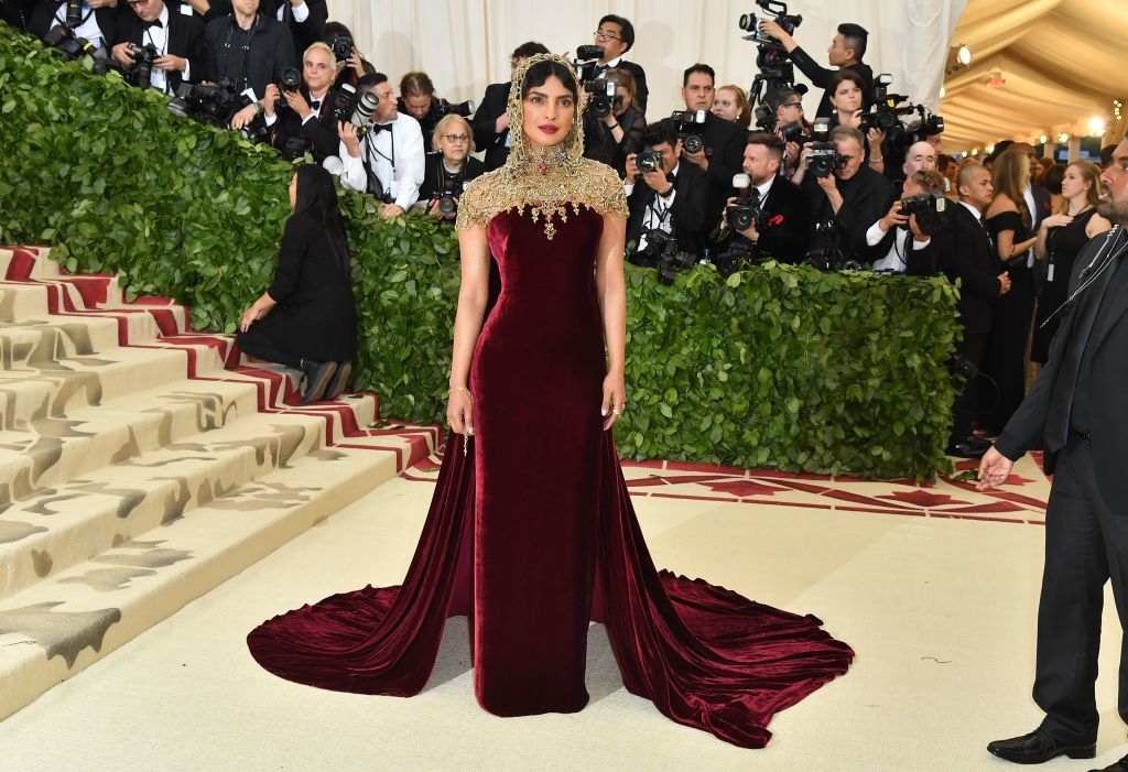 Priyanka Chopra in a velvet gown with a gold beaded neckline at an event, photographers in the background