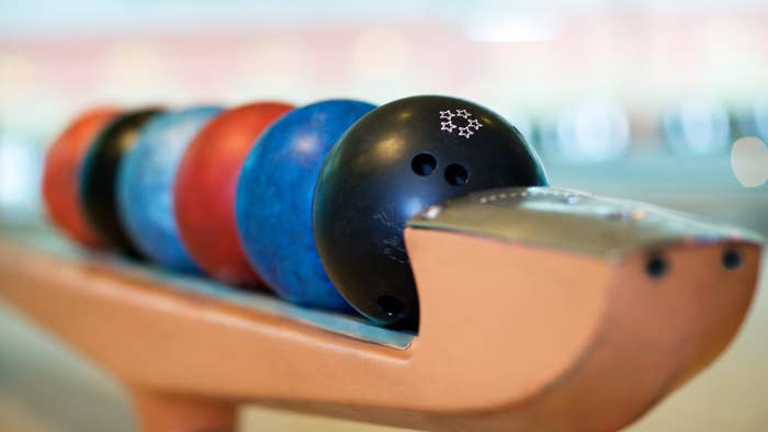 Row of bowling balls on rack in bowling alley, with focus on a black ball in the foreground