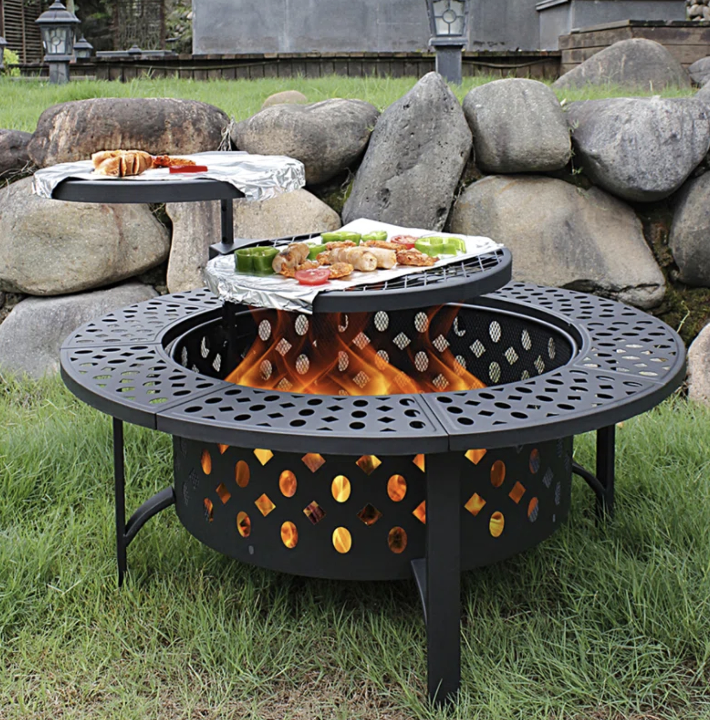 The open-design fire pit with a grill top cooking food and second grill grate resting in background