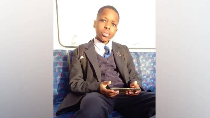 A boy in a school uniform sits on a train, holding a handheld gaming device