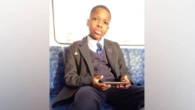 A boy in a school uniform sits on a train, holding a handheld gaming device