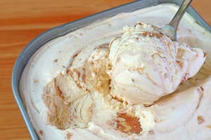 A spoon scooping vanilla ice cream with caramel swirls from a container